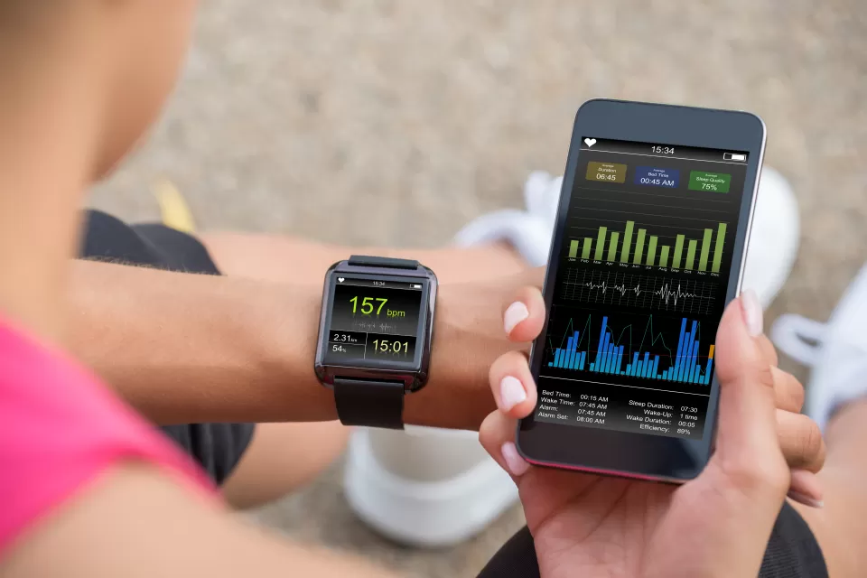 Close-up of person holding up phone and looking at their smart watch displaying fitness data